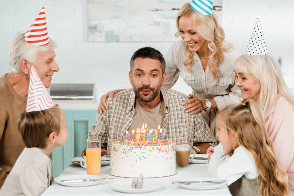 A 30-year-old man blows out candles on a birthday cake surrounded by his family.