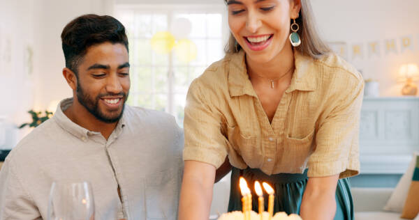 A couple celebrates a birthday at home with cake, a kiss, and a surprise gift from the wife to her husband, enjoying the party and their time together.