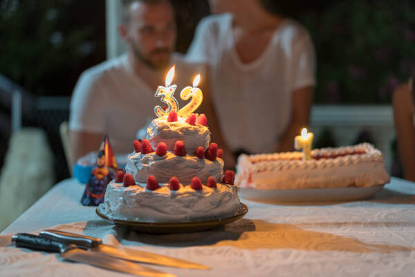 A focused view of a birthday cake with '32' candles, while the birthday boy sits celebrating in the background.