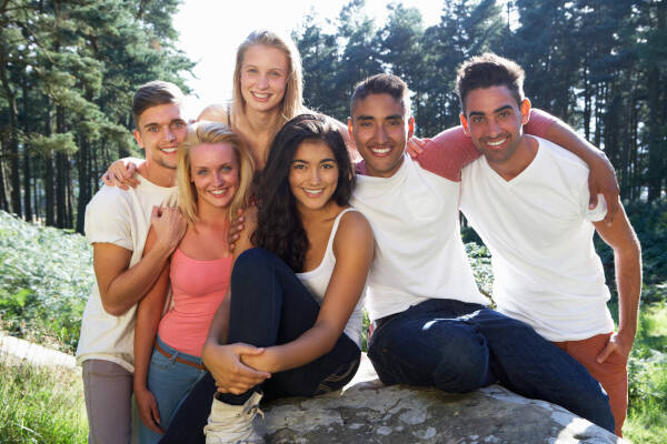 A group of young people posing for a photo outdoors in nature, all smiling.