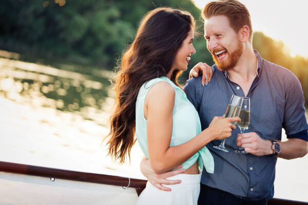 A happy, smiling couple in love dances and flirts while holding glasses filled with white wine.