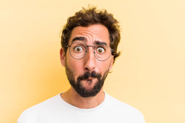 A man in spectacles pulls a funny face as he looks at the camera against a yellow background