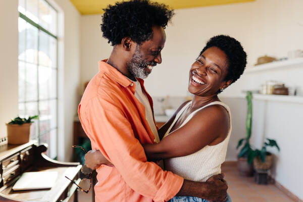 A mature couple shares a loving embrace in their kitchen at home, their genuine smiles and affectionate bond reflecting a happy and harmonious relationship.