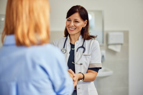 A smiling female doctor looks happy while holding her patient's hands.