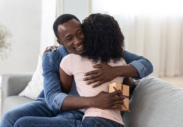 A smiling man holding a present hugs his wife, thanking her for the wonderful surprise in their home.