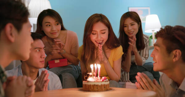 A young woman makes a wish in front of her birthday cake, surrounded by her friends.