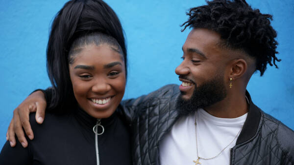 Adult siblings hugging each other and posing for a photo, smiling against a blue backdrop.