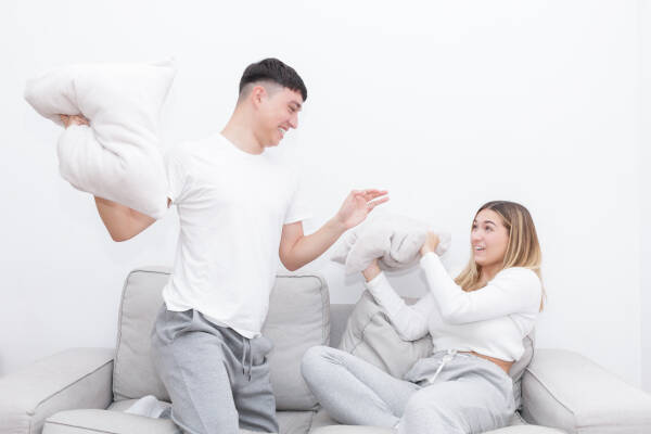 Boyfriend and girlfriend pillow fighting on the sofa at home.