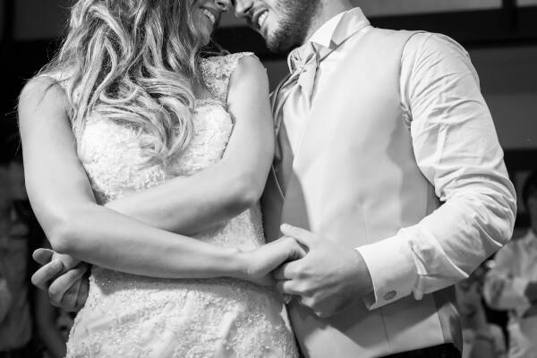 Bride and groom during their first dance, standing side by side holding hands and smiling.