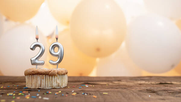 Cake with number '29' candles atop on a wooden table, with balloons in the background.