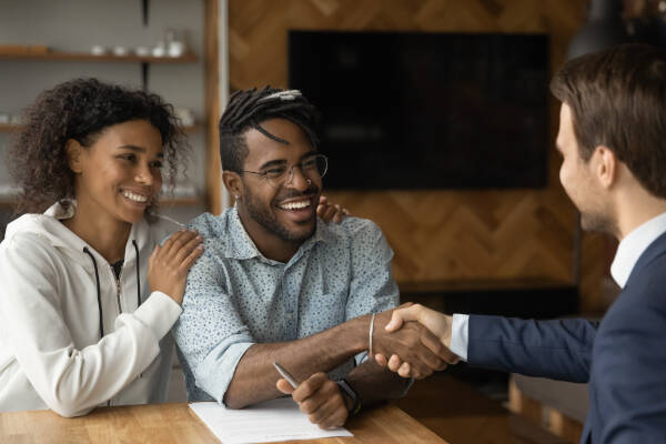 Close-up of a happy couple and a businessman shaking hands at a meeting. The man is smiling as he seals the deal with a handshake.