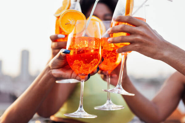 Close-up of female and male hands toasting orange cocktails outdoors.