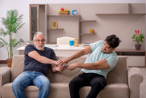 Father and adult son fighting over the remote on the sofa at home, both wearing funny expressions.