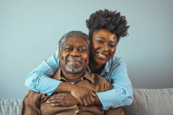 Father and daughter share a hug on the sofa at home, both smiling.