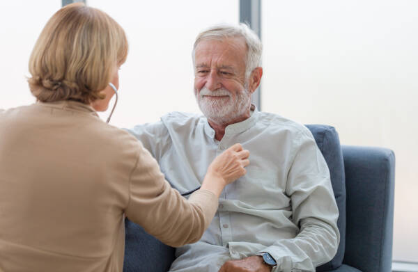 Focus on a female professional doctor holding a stethoscope while examining an elderly male patient.