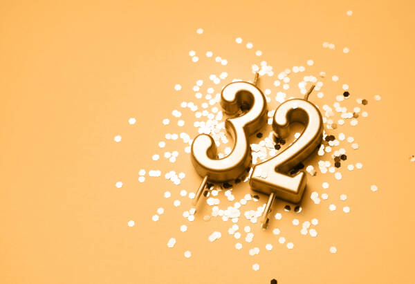 Golden '32' candles against a golden background surrounded by confetti.