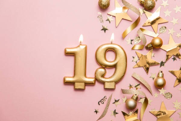 Golden number 19 candles adorned with gold stars and baubles against a pink backdrop.