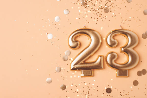 Golden number 23 candles on a peach background surrounded by confetti.