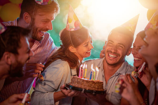 Group of friends celebrating a birthday together outdoors in party hats, smiling with a cake.