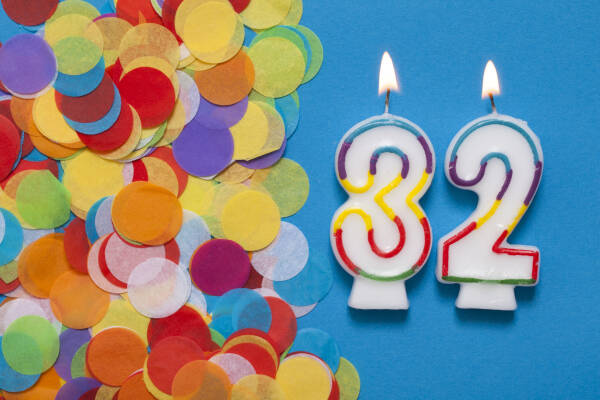 Number '32' candles are lit next to confetti against a blue background.