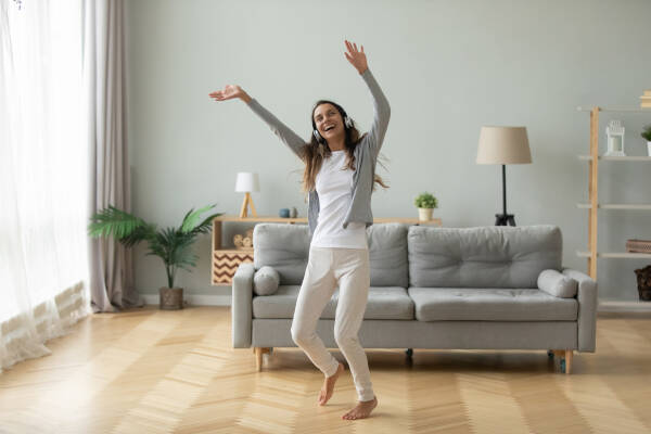 Overjoyed woman in her 30s wearing headphones, dancing in a modern living room at home.