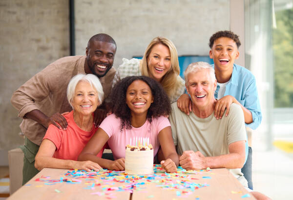 Portrait of a three-generation family at home celebrating their 19-year-old daughter's birthday with a cake at the table.