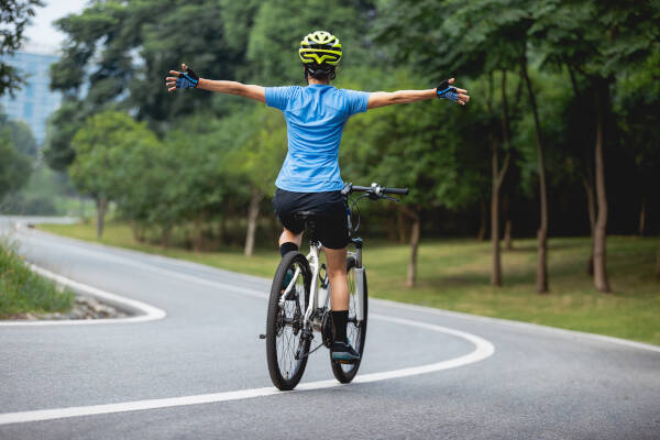 Person riding a bike without using hands, arms stretched out wide cycling down an wide open road.