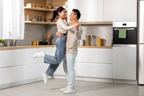 Romantic lovers dance a waltz in the kitchen, with a cheerful middle-aged husband lifting his happy young wife as they enjoy their time together at home.