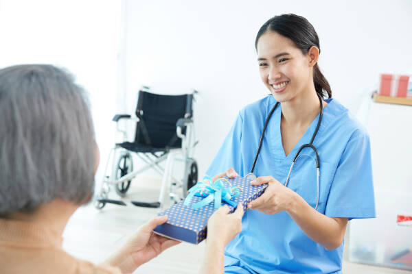 Senior woman handing a birthday present, wrapped in blue  polka dot paper with a blue ribbon, to her smiling female doctor.