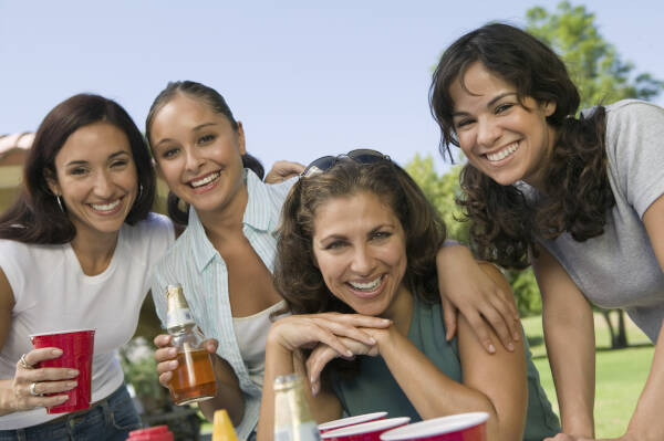 Sisters posing for a photo with their mother outside at a family party, holding drinks and smiling.
