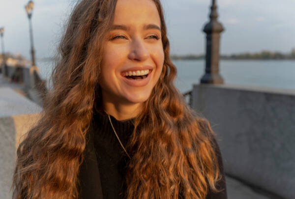 The 23-year-old woman laughs as she stands outside with the sun setting in the background.
