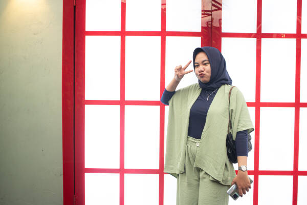 The 23-year-old woman pulls a cheeky face and holds up a peace sign as she stands in front of red windows.
