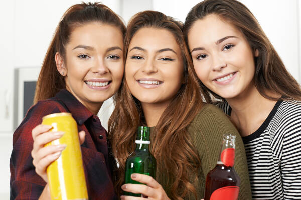 Three female friends pose for a photo, holding up their drinks and smiling