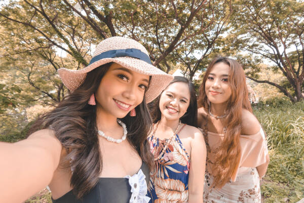 Three friends pose for a selfie, smiling as they stand outdoors surrounded by grass and trees.