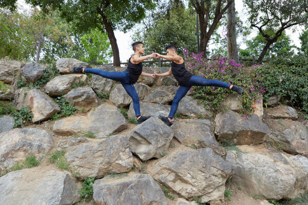 Twin brothers practice a dance, balancing impressively on a rocky hill in nature.