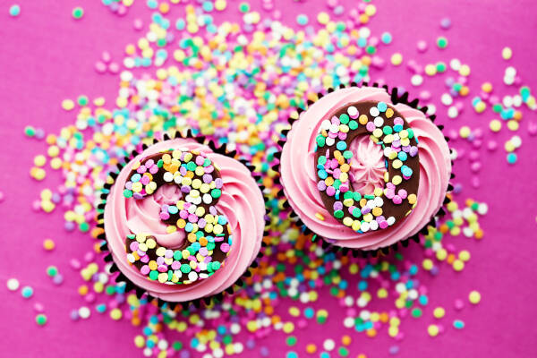 Two pink cupcakes with '30' on them, covered in sprinkles, on a pink background.