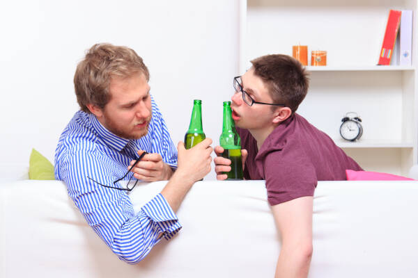 Two young male friends in their early 20s drinking on the sofa at one of their homes.