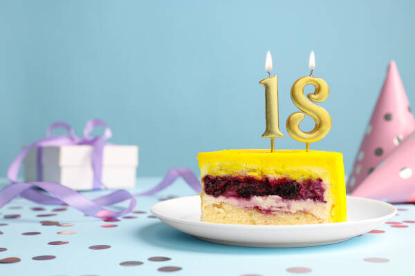 Yellow slice of cake with '18' candles atop against a blue background, next to a gift box and party hat.