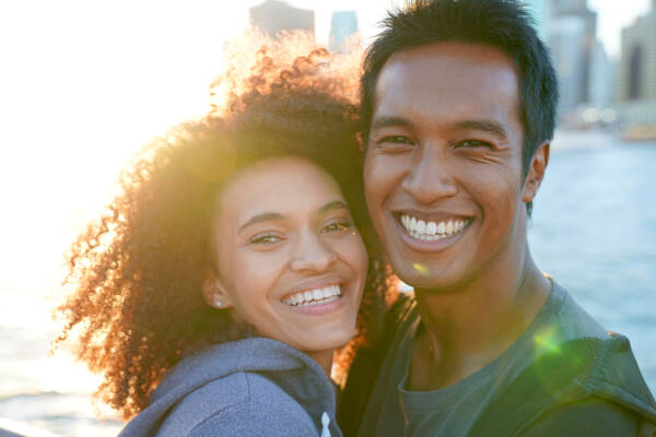 Young 30-year-old couple smiling widely as they stand in Manhattan at sunset.