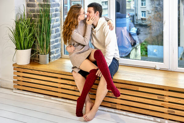 Young couple sitting on a windowsill in a modern home, with the woman on the man's lap, looking into each other's eyes.