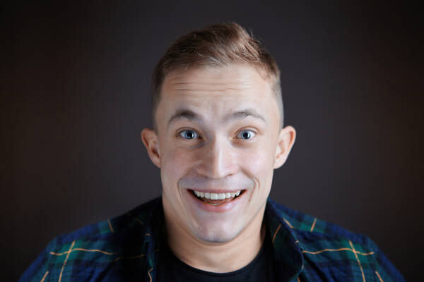 Zoomed-in shot of a 22-year-old man smiling widely against a black backdrop.