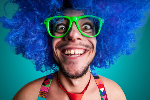 Zoomed-in shot of a man wearing green glasses and a blue wig, pulling a funny face.