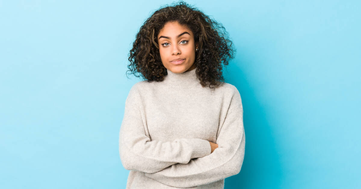 Woman starely blankly with her arms folded infront of her, set against a blue background.