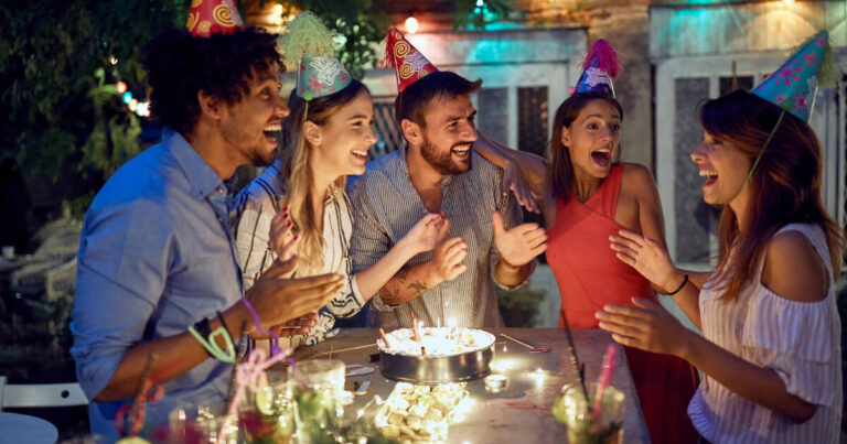 A group of cheerful friends celebrating a birthday at an open-air party on a beautiful summer night.