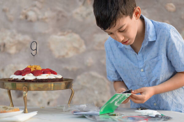 A boy opening presents at a table with a birthday cake topped with strawberries and a "9" candle.