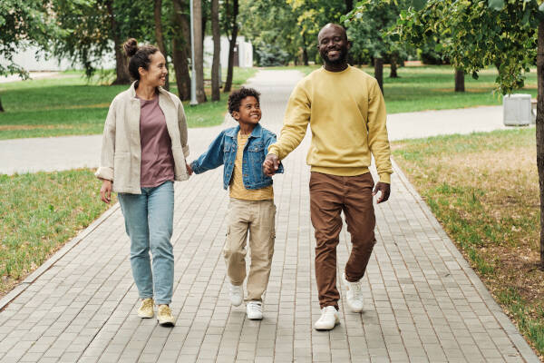 A happy family strolling hand in hand with their young son in the park, enjoying a leisurely walk together through the streets.