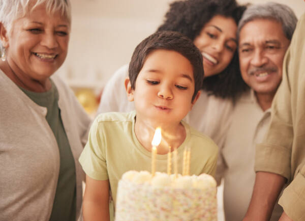 A young boy blowing out candles on a birthday cake, surrounded by smiling family members.