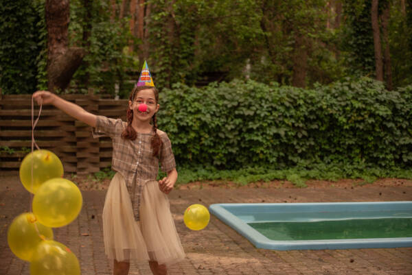 An 11-year-old girl celebrating her birthday with colorful balloons, set against the backdrop of a pool.