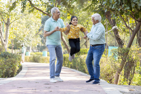 Two elderly men enjoying a playful moment with their granddaughter in the park, radiating joy and creating cherished memories together.