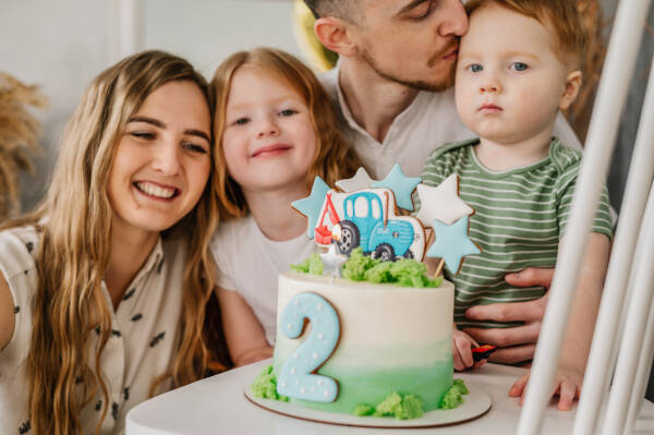 Zoomed-in shot of dad with his three kids sitting at a table with a 2nd birthday cake.